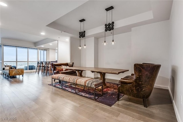 living area with wood finished floors, recessed lighting, a raised ceiling, and baseboards