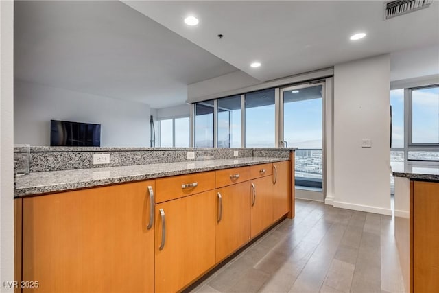 kitchen featuring light stone counters, recessed lighting, visible vents, and wood finished floors