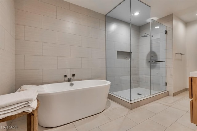 bathroom with a stall shower, tile patterned floors, tile walls, and a soaking tub