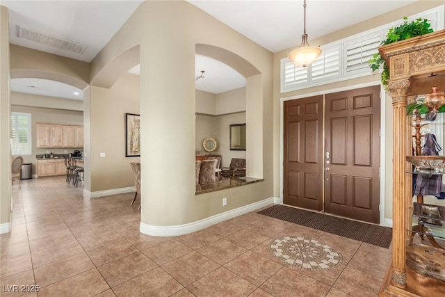 entryway with arched walkways, light tile patterned flooring, visible vents, and baseboards