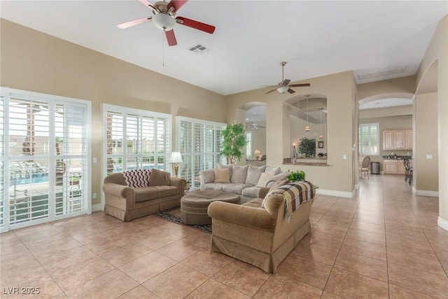 living area with baseboards, visible vents, arched walkways, a ceiling fan, and light tile patterned flooring