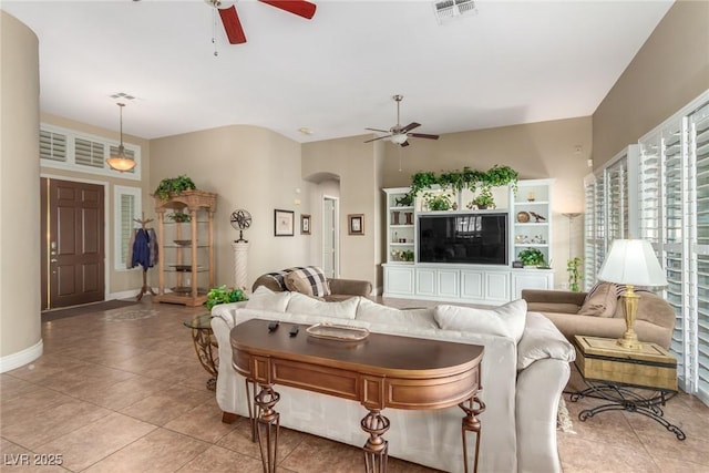 living room with arched walkways, light tile patterned floors, visible vents, ceiling fan, and baseboards