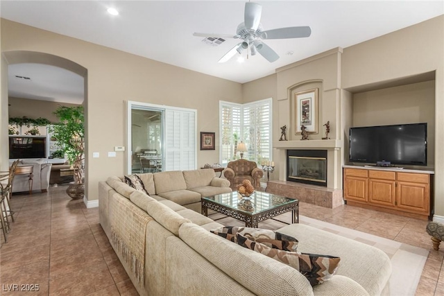 living area featuring visible vents, baseboards, ceiling fan, a premium fireplace, and light tile patterned flooring