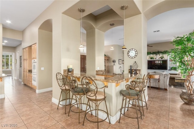 kitchen featuring arched walkways, light tile patterned floors, a sink, white oven, and a kitchen bar