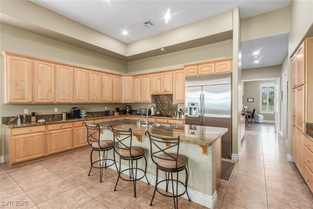 kitchen with built in fridge, a breakfast bar, dark stone countertops, and light brown cabinetry