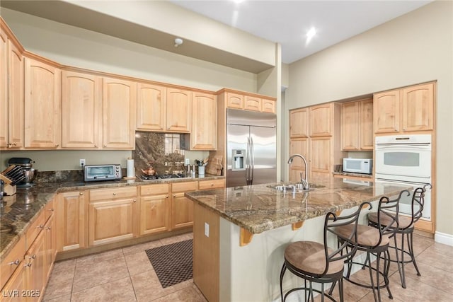 kitchen featuring a breakfast bar area, appliances with stainless steel finishes, dark stone countertops, light brown cabinetry, and a sink