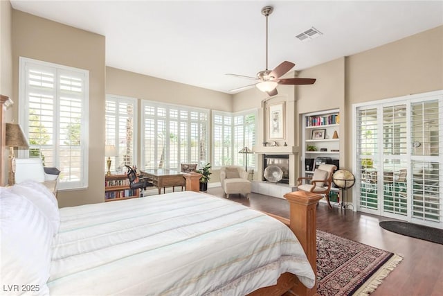 bedroom with wood finished floors, a ceiling fan, visible vents, access to exterior, and a tiled fireplace