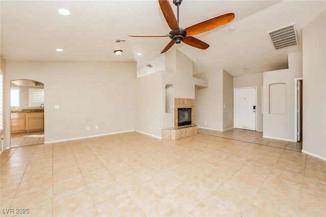 unfurnished living room with lofted ceiling, a ceiling fan, visible vents, baseboards, and a tiled fireplace