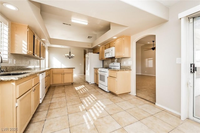 kitchen with a tray ceiling, white appliances, a peninsula, and light brown cabinetry