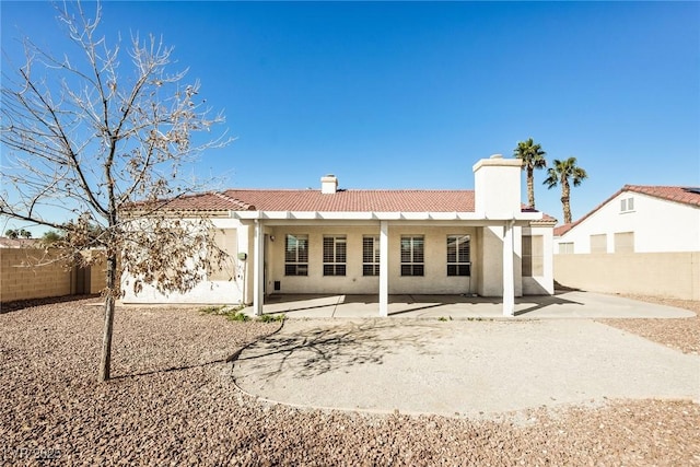 rear view of house with a patio, fence, a tiled roof, stucco siding, and a chimney