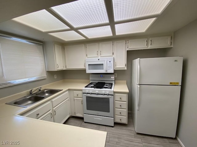 kitchen with white appliances, light countertops, a sink, and baseboards