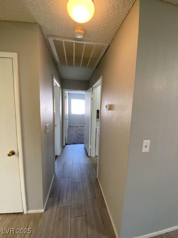 hallway featuring visible vents, a textured ceiling, baseboards, and wood finished floors