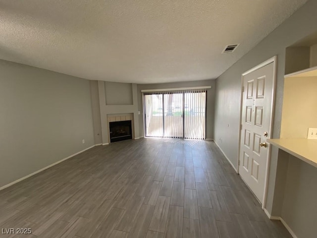 unfurnished living room with a textured ceiling, dark wood-style flooring, a fireplace, and visible vents