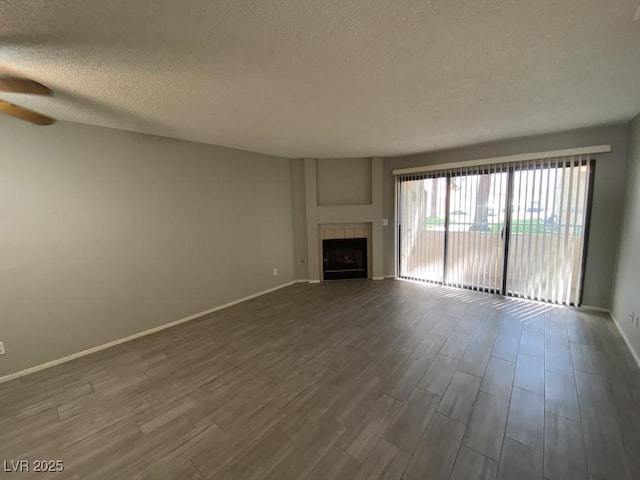 unfurnished living room featuring a tile fireplace, dark wood-style flooring, a textured ceiling, and baseboards