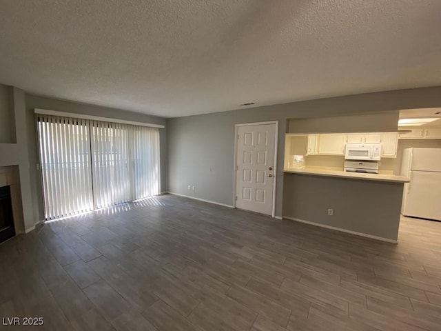 unfurnished living room with a textured ceiling, dark wood-style flooring, a fireplace, and baseboards