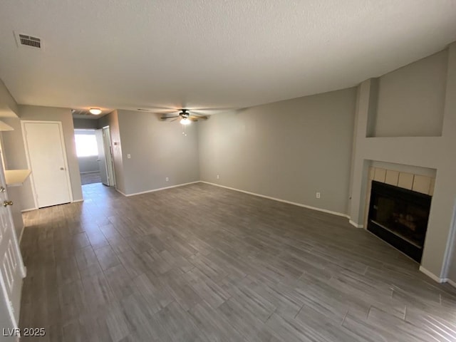 unfurnished living room featuring ceiling fan, dark wood finished floors, a tile fireplace, and visible vents