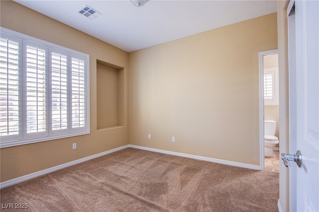 empty room with carpet floors, a wealth of natural light, visible vents, and baseboards