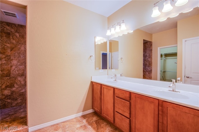 full bath featuring double vanity, tiled shower, a sink, and baseboards