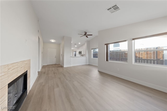 unfurnished living room featuring baseboards, visible vents, a tiled fireplace, lofted ceiling, and light wood-style floors