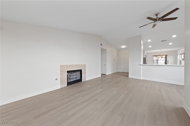 unfurnished living room with visible vents, vaulted ceiling, light wood-style floors, a fireplace, and ceiling fan with notable chandelier