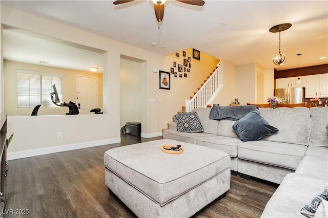 living room featuring dark wood-style flooring, ceiling fan, baseboards, and stairs