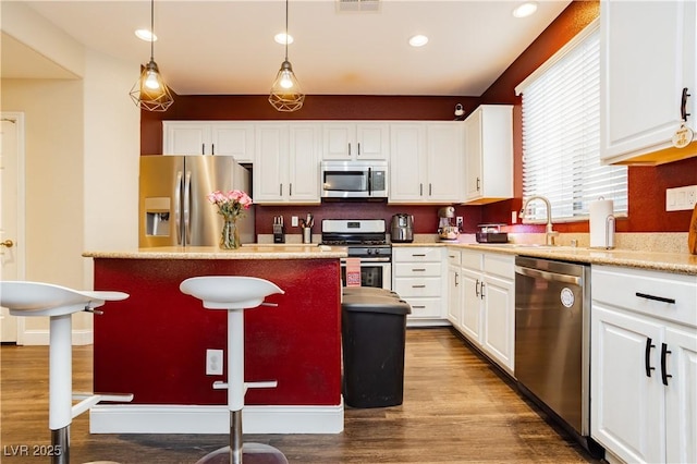 kitchen featuring dark wood-style flooring, a kitchen island, white cabinetry, appliances with stainless steel finishes, and pendant lighting