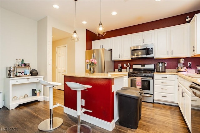 kitchen with recessed lighting, stainless steel appliances, wood finished floors, a kitchen island, and white cabinetry