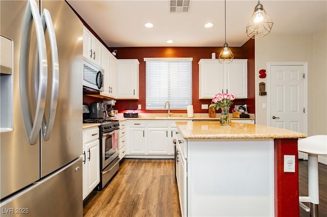 kitchen featuring visible vents, a kitchen island, appliances with stainless steel finishes, wood finished floors, and a sink