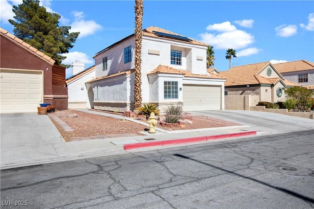 mediterranean / spanish-style home with a tile roof, stucco siding, solar panels, an attached garage, and driveway