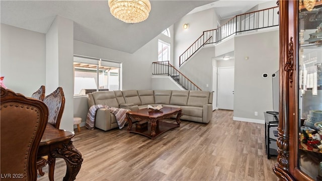 living room featuring a high ceiling, an inviting chandelier, wood finished floors, baseboards, and stairs