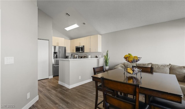 kitchen featuring a peninsula, dark wood-type flooring, light countertops, appliances with stainless steel finishes, and light brown cabinetry