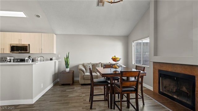 dining space with dark wood finished floors, lofted ceiling, visible vents, a tiled fireplace, and baseboards