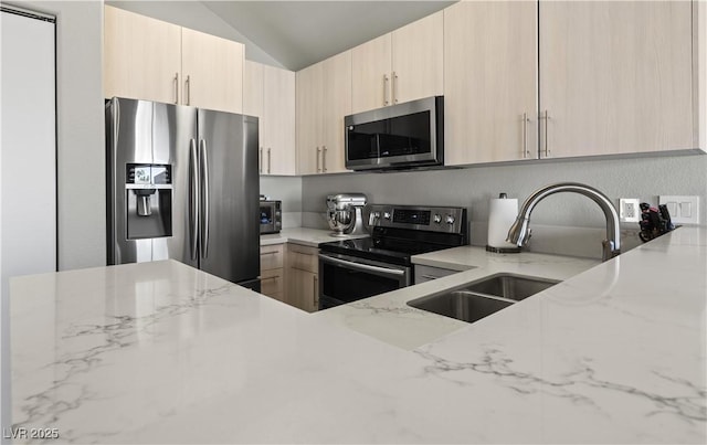 kitchen featuring light stone counters, stainless steel appliances, a sink, vaulted ceiling, and light brown cabinetry