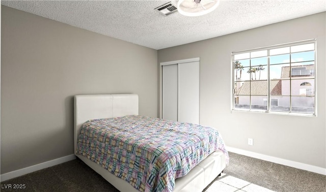 bedroom featuring visible vents, baseboards, carpet, a textured ceiling, and a closet