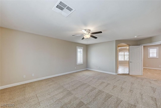 spare room featuring baseboards, visible vents, arched walkways, light colored carpet, and ceiling fan