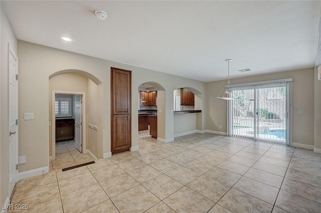 empty room featuring arched walkways, light tile patterned flooring, visible vents, and baseboards