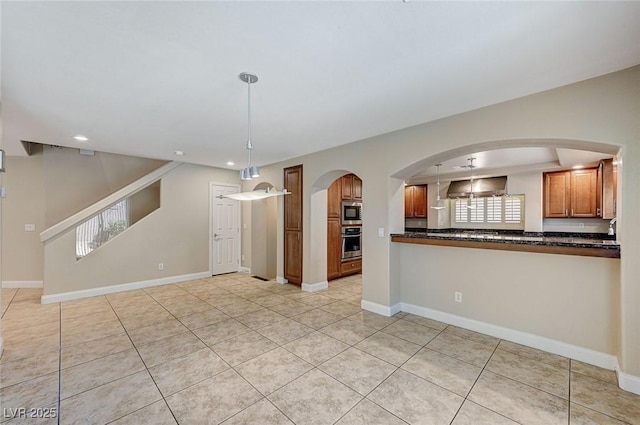 kitchen with baseboards, appliances with stainless steel finishes, brown cabinetry, dark countertops, and decorative light fixtures