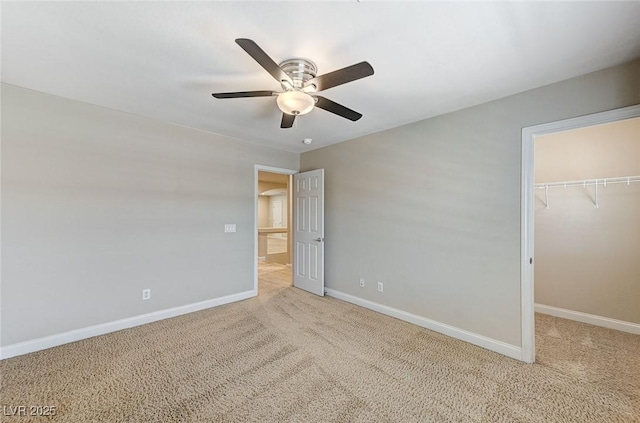 unfurnished bedroom with a walk in closet, a closet, a ceiling fan, carpet flooring, and baseboards