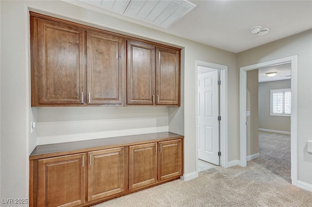 interior space with baseboards, brown cabinets, and light colored carpet