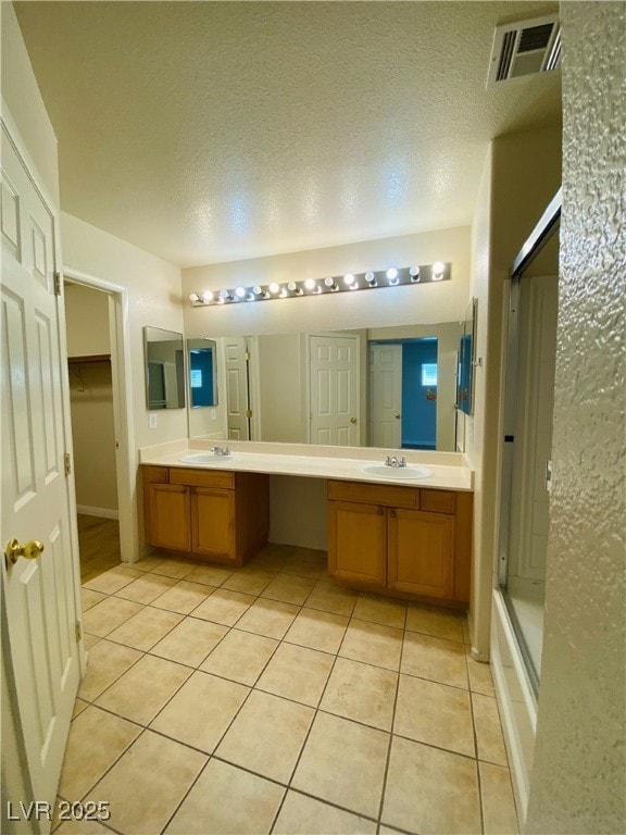 full bathroom with double vanity, visible vents, a shower with shower door, a sink, and tile patterned floors