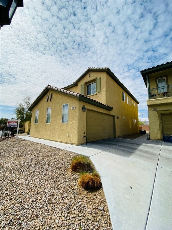 view of home's exterior with a garage, concrete driveway, a tiled roof, and stucco siding