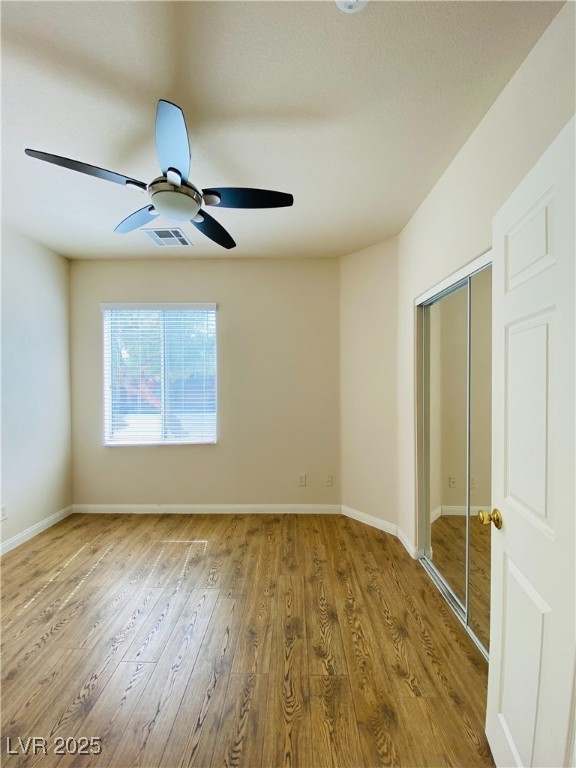 unfurnished bedroom featuring baseboards, visible vents, a ceiling fan, wood finished floors, and a closet