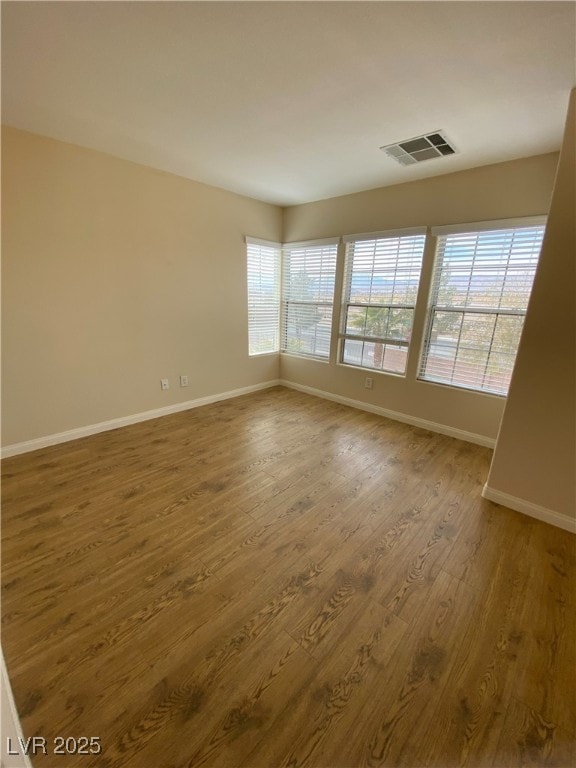 empty room with baseboards, visible vents, and wood finished floors