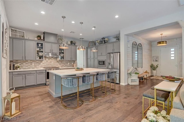 kitchen featuring decorative backsplash, a breakfast bar area, appliances with stainless steel finishes, gray cabinetry, and light countertops