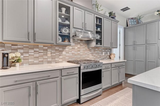 kitchen with under cabinet range hood, visible vents, gray cabinets, stainless steel range with gas cooktop, and tasteful backsplash