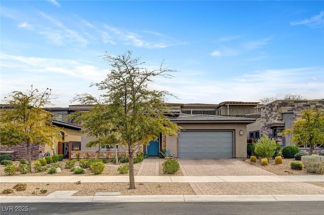 view of front of house featuring decorative driveway, an attached garage, and stucco siding