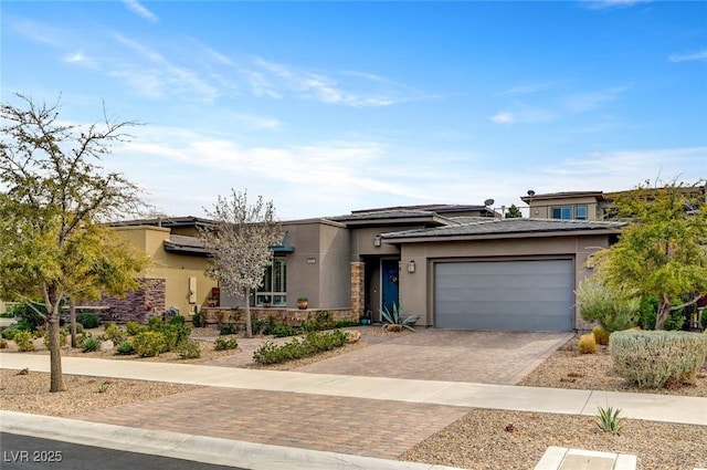 view of front facade with a garage, decorative driveway, stone siding, and stucco siding