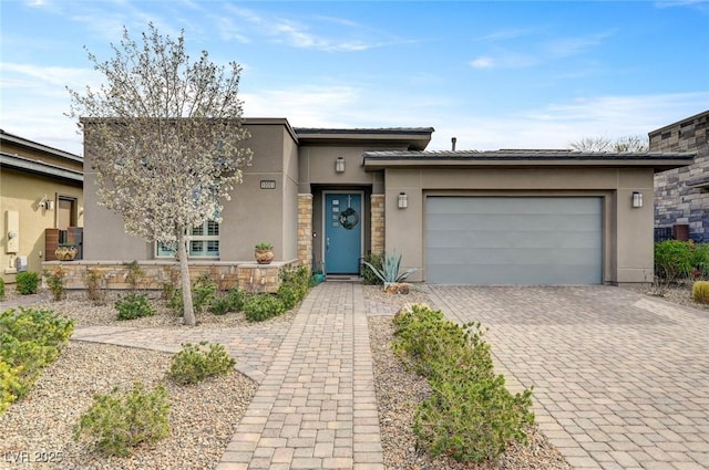 view of front of home featuring decorative driveway, a garage, stone siding, and stucco siding