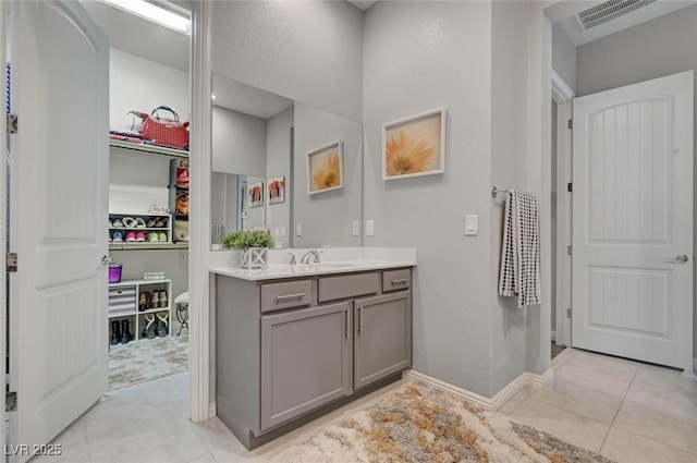 bathroom with visible vents, baseboards, tile patterned flooring, a walk in closet, and vanity