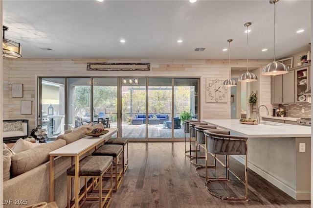 kitchen featuring a breakfast bar area, dark wood-type flooring, a sink, open floor plan, and backsplash